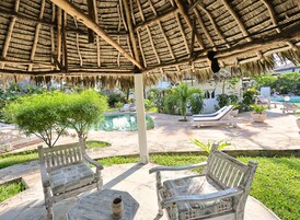 Un espacio al aire libre techado con piscina, sillones de descanso y una estructura de techo de paja.