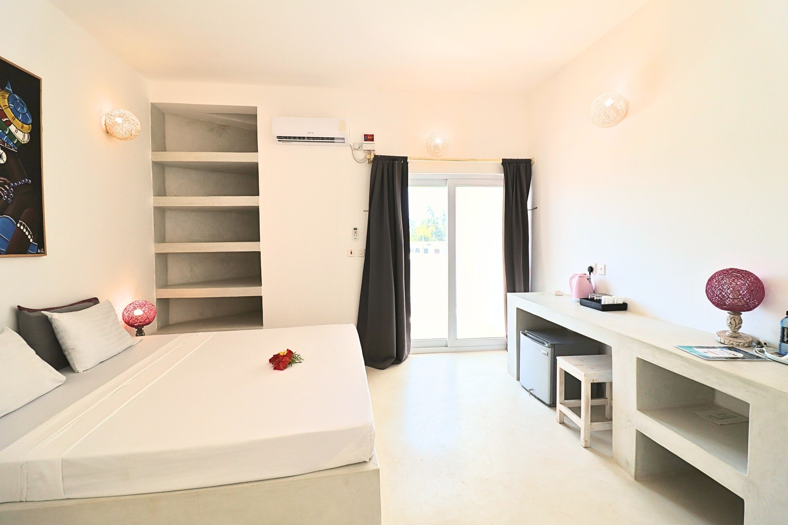 Une chambre d’hôtel avec un lit, un bureau, une chaise, une étagère et une fenêtre.