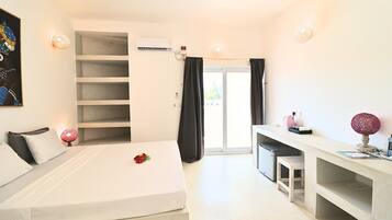 Une chambre d’hôtel avec un lit, un bureau, une chaise, une étagère et une fenêtre.