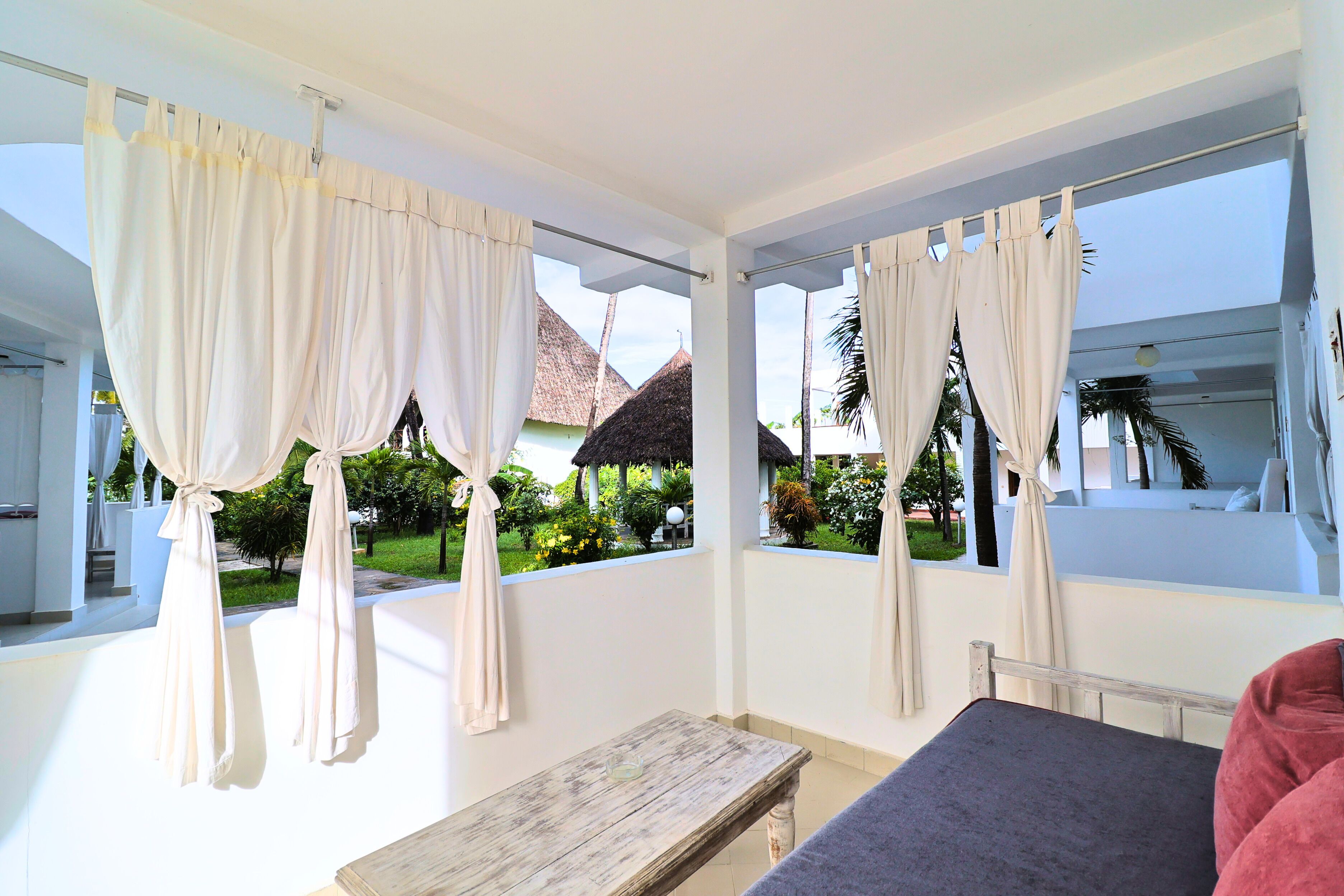 A room with a bed, a wooden table, and large windows with curtains.