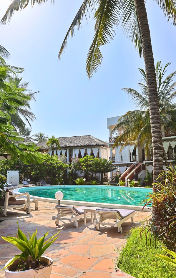 A pool area with lounge chairs, a thatched-roof building, and palm trees. - Watamu Ascot Hotel (Watamu)