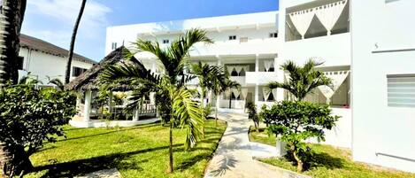 Un edificio blanco con un patio central, rodeado de palmeras y un sendero de piedra.