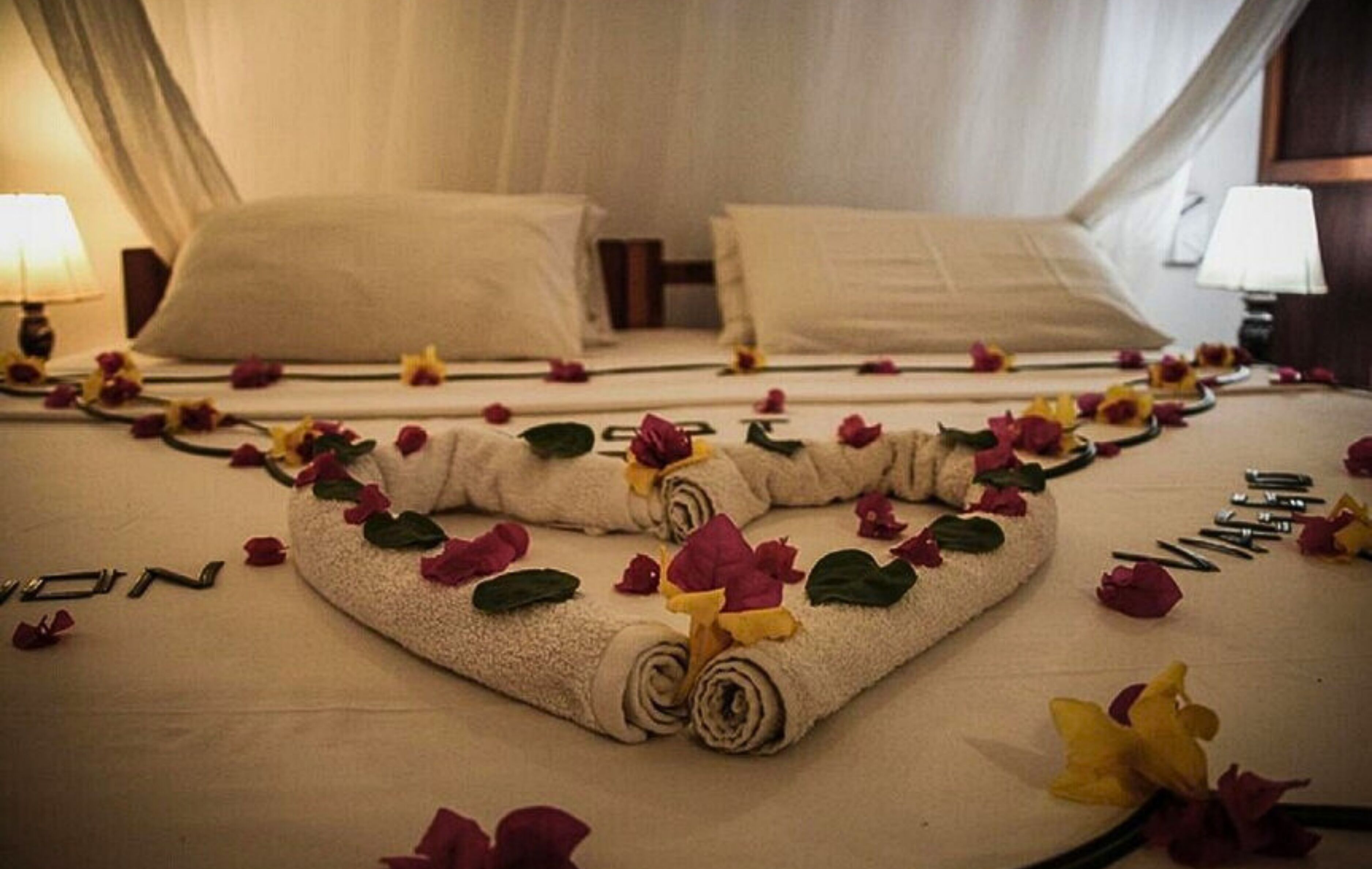 A neatly made bed with rolled towels and scattered flowers.