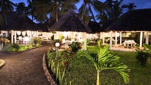Un resort con capanne a tetto di paglia, palme e un giardino curato.