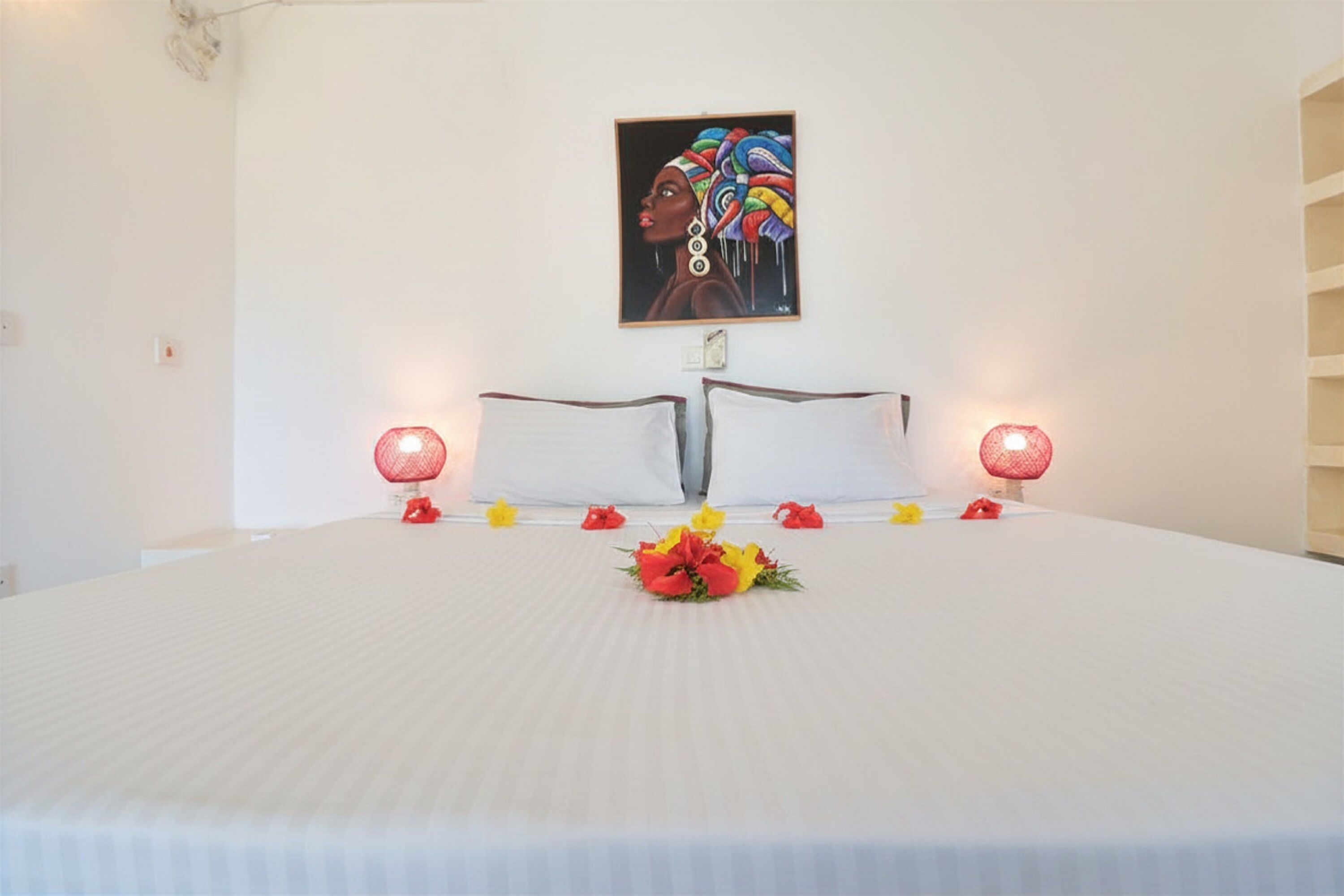 A neatly made bed with white linens, a floral centerpiece, and two wall-mounted lamps.