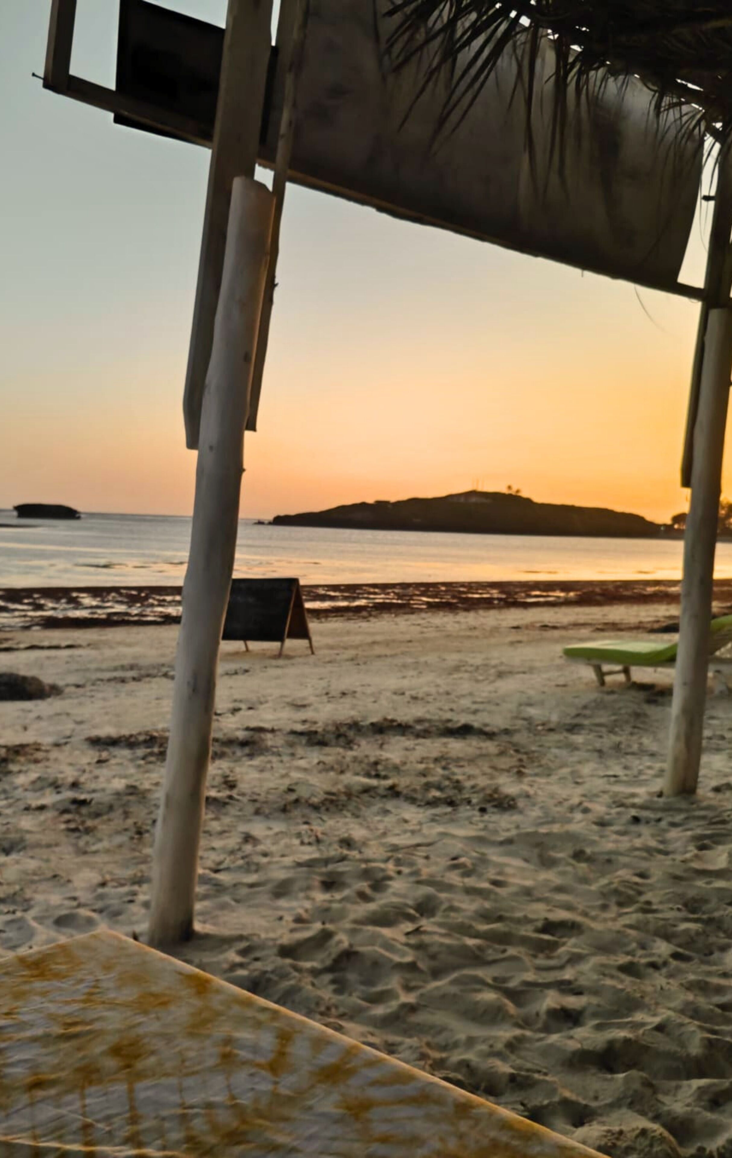 Una playa con una estructura de madera, una pizarra y una silla de lounge verde.