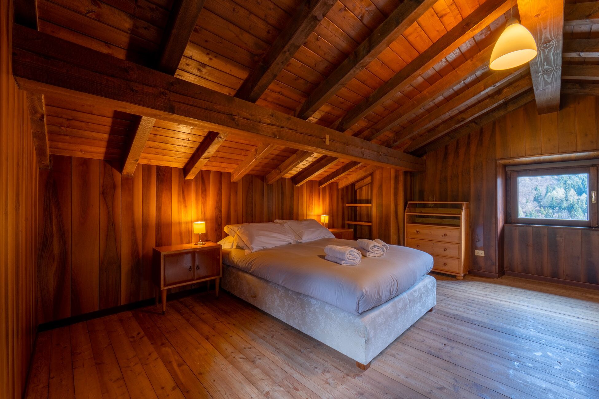 A cozy wooden cabin bedroom with a bed, nightstands, and a window.