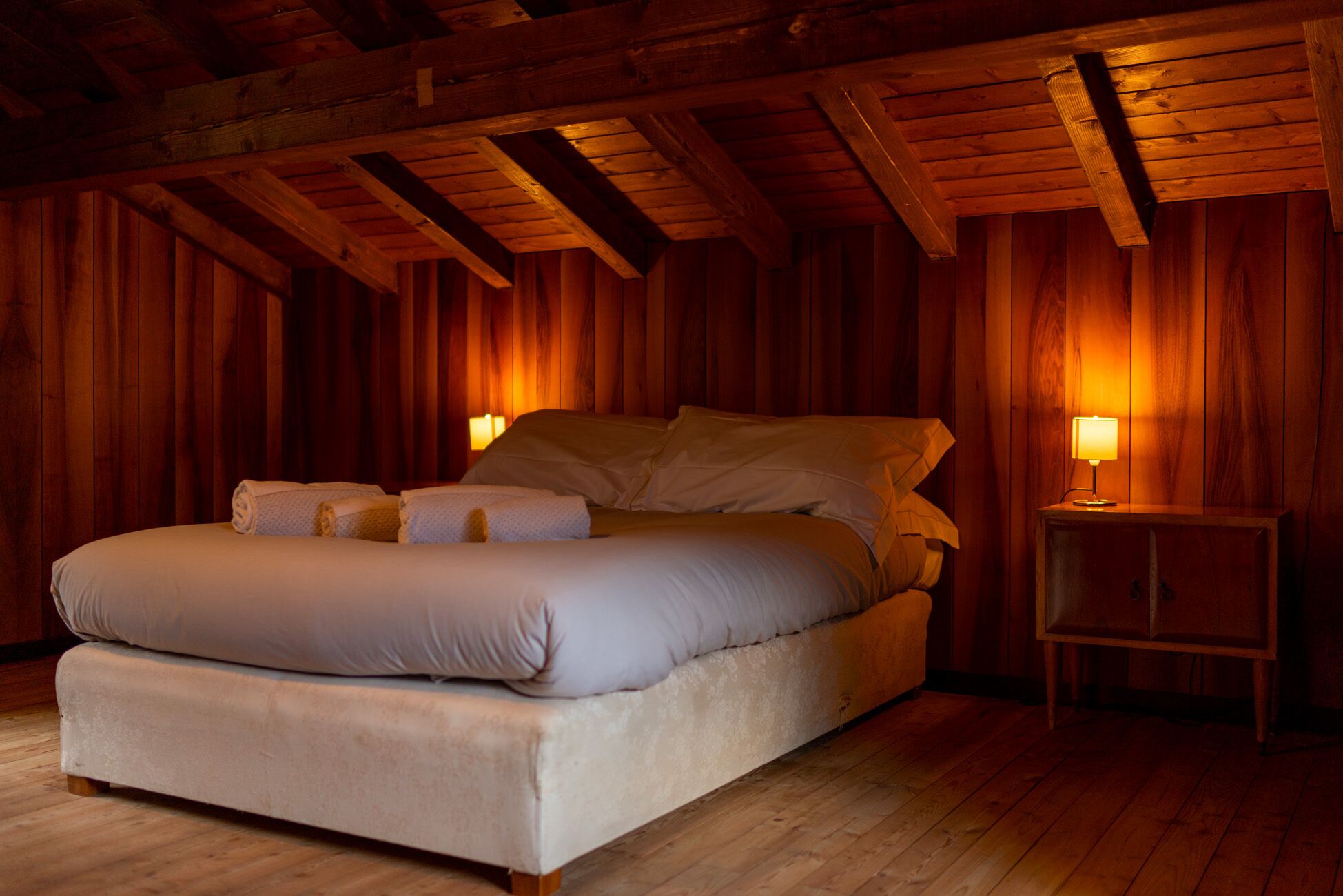 Une chambre aux murs lambrissés, avec un lit, des oreillers et une table de chevet sur laquelle se trouve une lampe.