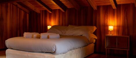 Une chambre aux murs lambrissés, avec un lit, des oreillers et une table de chevet sur laquelle se trouve une lampe.