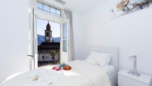 Ein Hotelzimmer mit Bett, Nachttisch, Fenster mit Blick auf einen Uhrturm und einer Anrichtung für das Frühstück auf dem Bett.