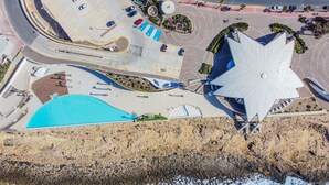 An aerial view of a coastal area with a large white building, a swimming pool, and a parking lot. - Modern Beautifull Pool And Sea Apt Qawra (St. Paul's Bay)