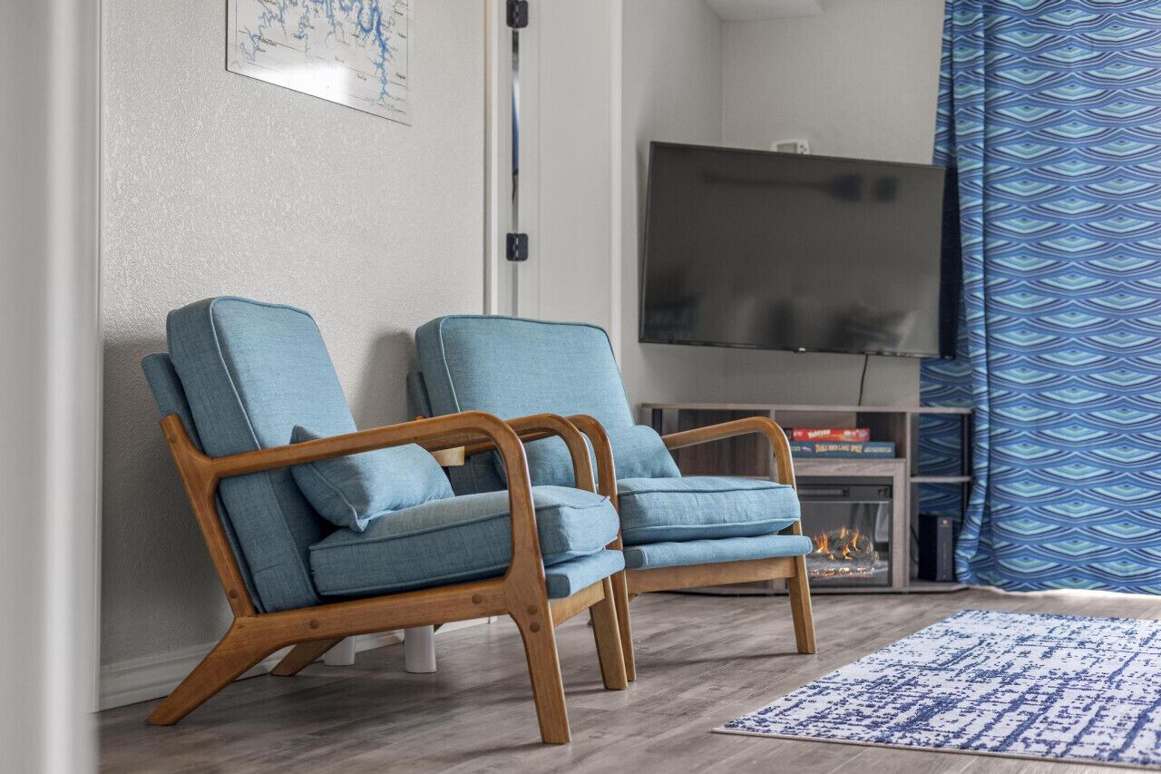 A living room with two blue armchairs, a flat-screen TV, and a patterned rug.