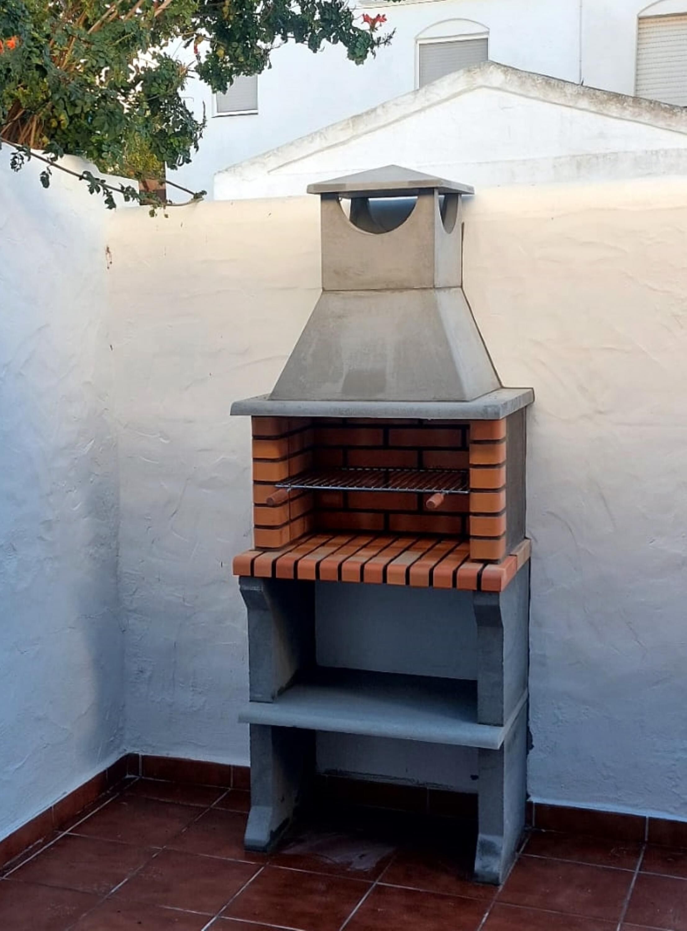 Een bakoven van baksteen met schoorsteen, tegen een witte muur op een betegeld terras.