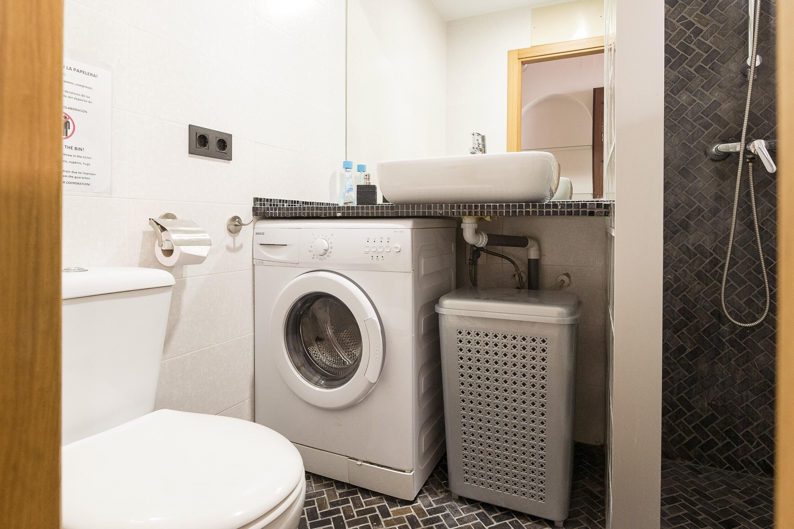A compact bathroom with a washing machine, a sink, and a shower.