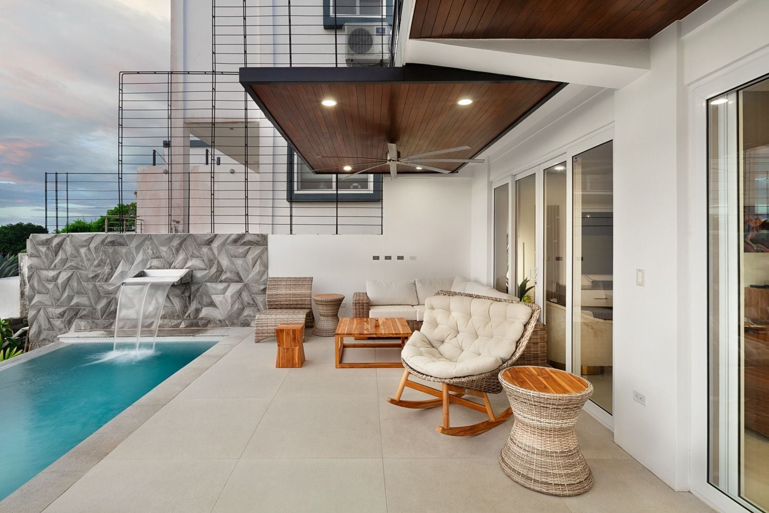 A modern outdoor living area with a pool, seating, and a waterfall feature.