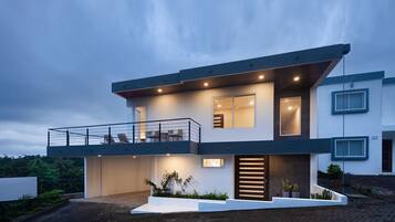 Una casa moderna de dos pisos con balcón, ventanas amplias y una entrada bien iluminada.