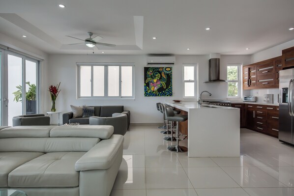 A modern kitchen with a central island, bar stools, and a dining area with a sofa. - Malibu At Pacific Marlin (San Juan del Sur)