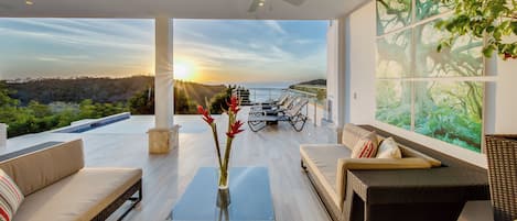 En moderne stue med havudsigt i solnedgang, en loftsvifte og et stort vindue med et naturmotiv.