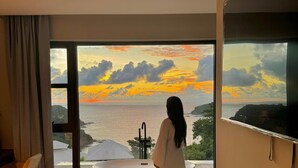 Un baño moderno con una bañera grande, un televisor montado en la pared y vista al mar al atardecer.