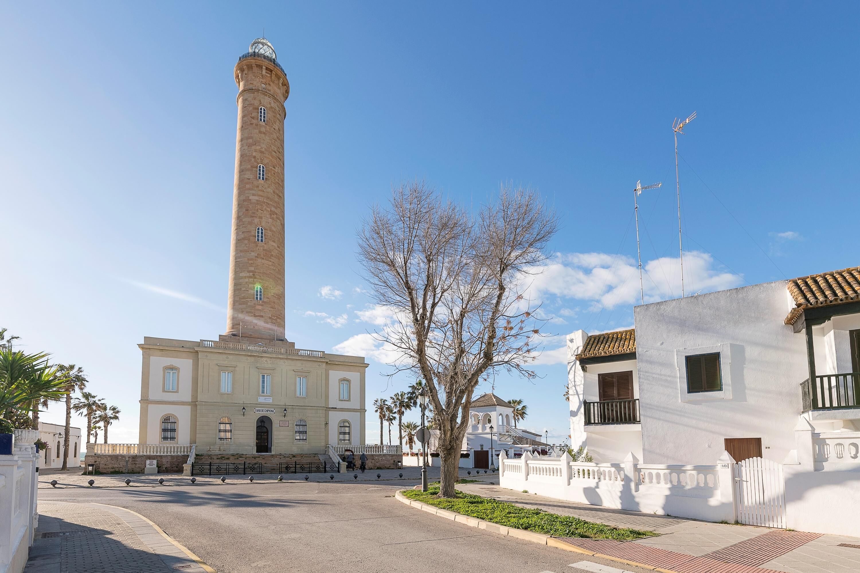 A historic building with a tall tower, a white building with balconies, and a clear blue sky.