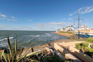 Vista costera con un paseo marítimo, olas del océano y un edificio con varias banderas.