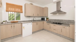 A modern kitchen with light wood cabinets, a granite countertop, a built-in dishwasher, a stove, and a window with blinds. - El Coto in Chiclana de la Frontera (Chiclana de la Frontera)