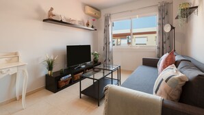 Ett modernt vardagsrum med en platt-TV, ett soffbord i glas, en soffa och ett vitt skrivbord.