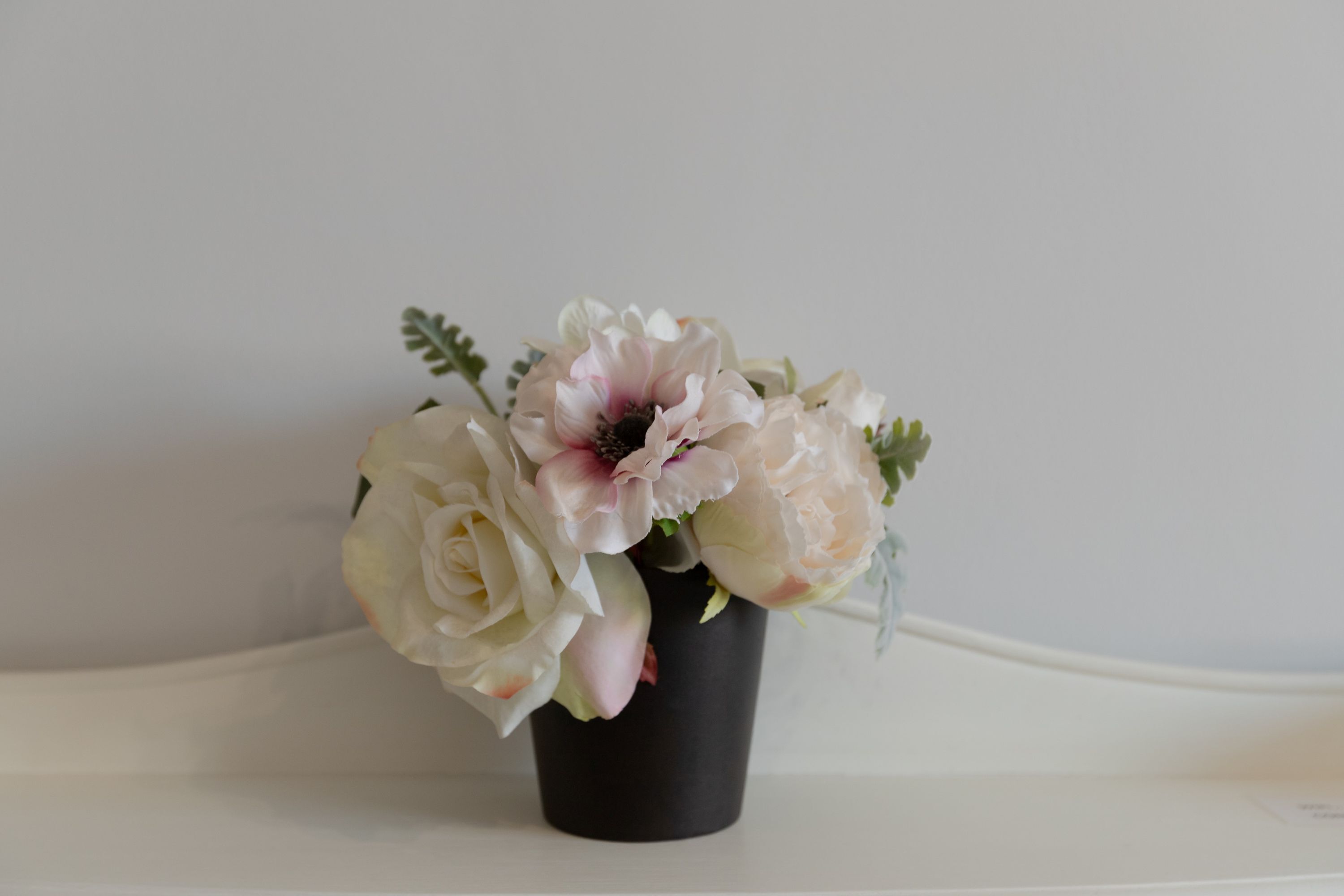 A black vase with a bouquet of white and light pink flowers on a white surface.