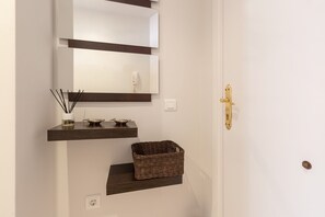 Un bagno con uno specchio, due ripiani, un cesto e una porta con maniglia dorata.