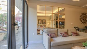 A living room with a beige sofa, a glass partition, and a view of the outside. - El Alcazar in Sevilla (Seville)