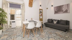 A modern living room with a dining area, featuring a patterned floor, a sofa, a table with chairs, and a wall-mounted shelf. - Casa Cuna in Arcos de la Frontera (Arcos de la Frontera)