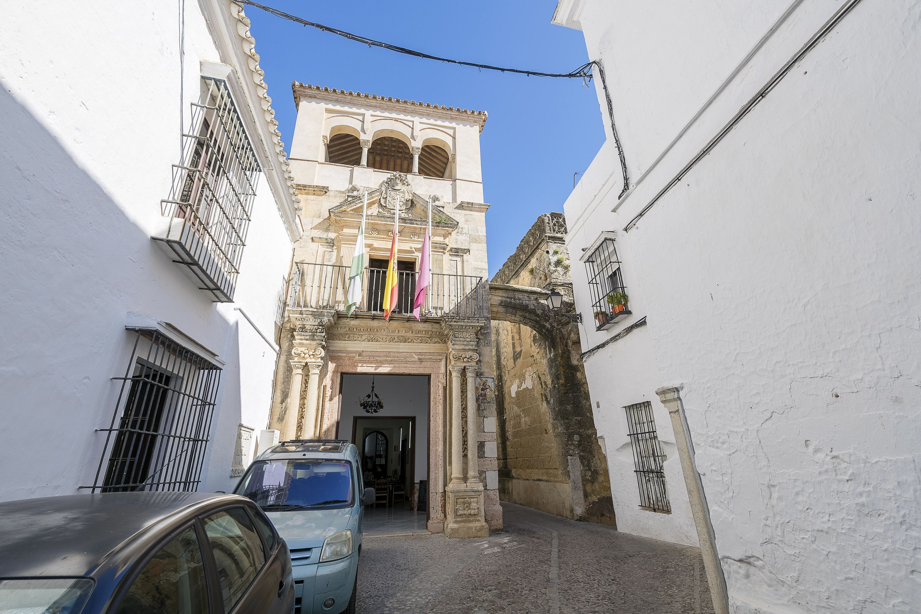 A narrow street with a historic building featuring a prominent entrance and a bell tower.
