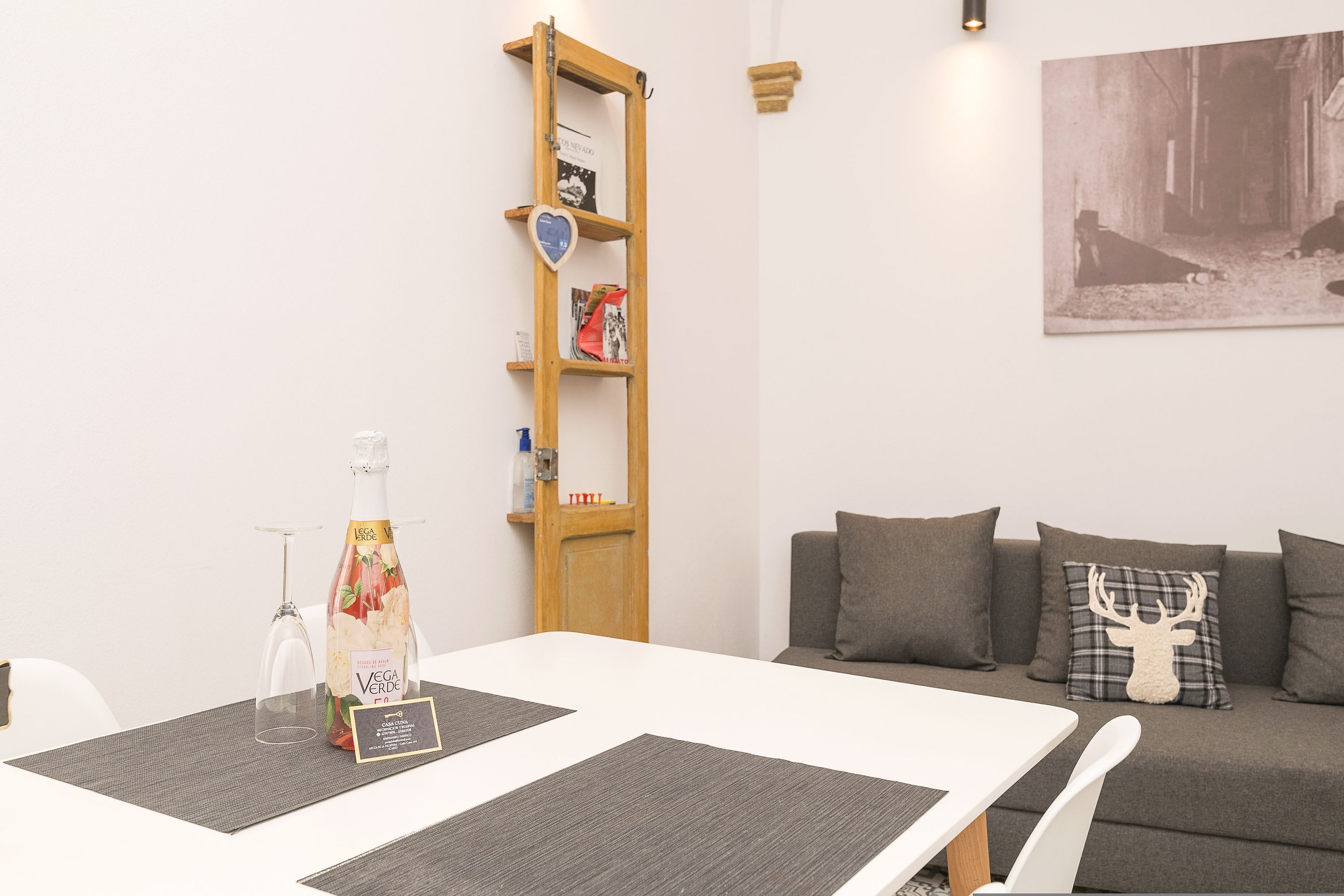 A modern living room with a white sofa, a wooden bookshelf, and a dining table with placemats.