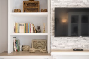 A bookshelf with books and decorative items, a framed picture with the word "HOME," and a television on a stone wall. - Rincon De Los Deseos (Grazalema)