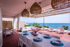 A terrace with white furniture, a table set for dining, and wicker ceiling lamps. - Villa Acqua Saracena by Wonderful Italy (Augusta)