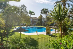 A swimming pool surrounded by lush greenery and palm trees, with a clear blue sky above. - Oasis Playero in Chiclana de la Frontera (Chiclana de la Frontera)