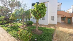 A courtyard with a white building, a tree with green foliage, and a brick pathway. - Oasis Playero in Chiclana de la Frontera (Chiclana de la Frontera)
