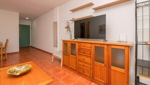 A spacious room with a wooden cabinet, a flat-screen TV, and a dining table with a decorative bowl. - Oasis Playero in Chiclana de la Frontera (Chiclana de la Frontera)