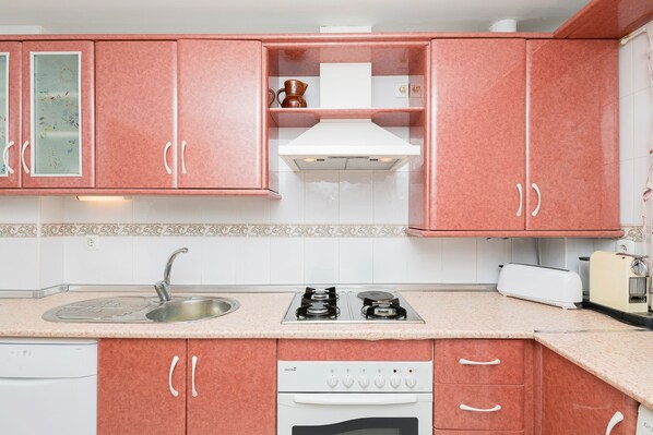 Uma cozinha com armários cor-de-rosa, um fogão branco e uma pia.
