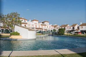 A swimming pool surrounded by white buildings with orange roofs, a clear blue sky, and a well-maintained lawn. - Rosamar in Chiclana de la Frontera (Chiclana de la Frontera)