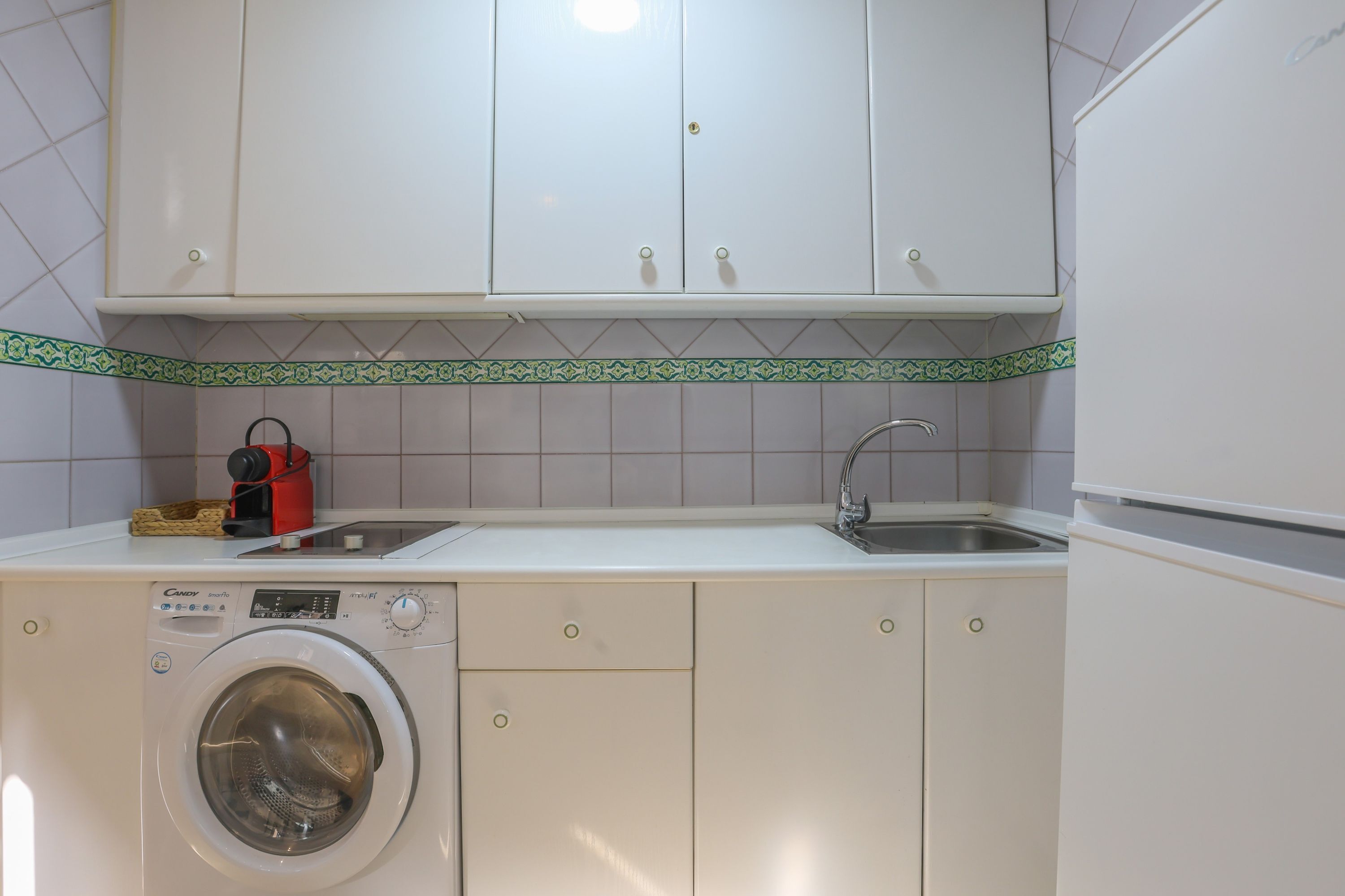 A compact kitchen with a washing machine, a sink, and a cabinet above.