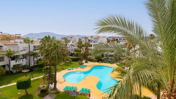 A resort with a large swimming pool, palm trees, and a view of the surrounding buildings. - Saladillo in Estepona (Estepona)