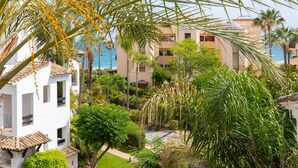 A white building with multiple balconies, surrounded by lush greenery and palm trees, overlooking a body of water. - Saladillo in Estepona (Estepona)