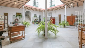 A spacious indoor area with a high ceiling, a staircase leading to an upper level, and multiple potted plants. - Posada De La Casa Del Pintor Hab Granada - Adults Only (Carmona)