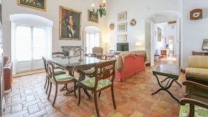 A spacious living room with a dining area, featuring a large wooden dining table, several chairs, a sofa, and a television. - Posada De La Casa Del Pintor Hab Granada - Adults Only (Carmona)