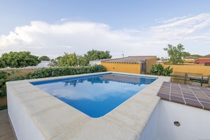 Une piscine rectangulaire dont les bords sont recouverts de carreaux, entourée d’un petit muret en pierre et d’une zone de terrasse également carrelée.