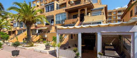 A multi-story hotel with balconies, outdoor seating, and potted plants.