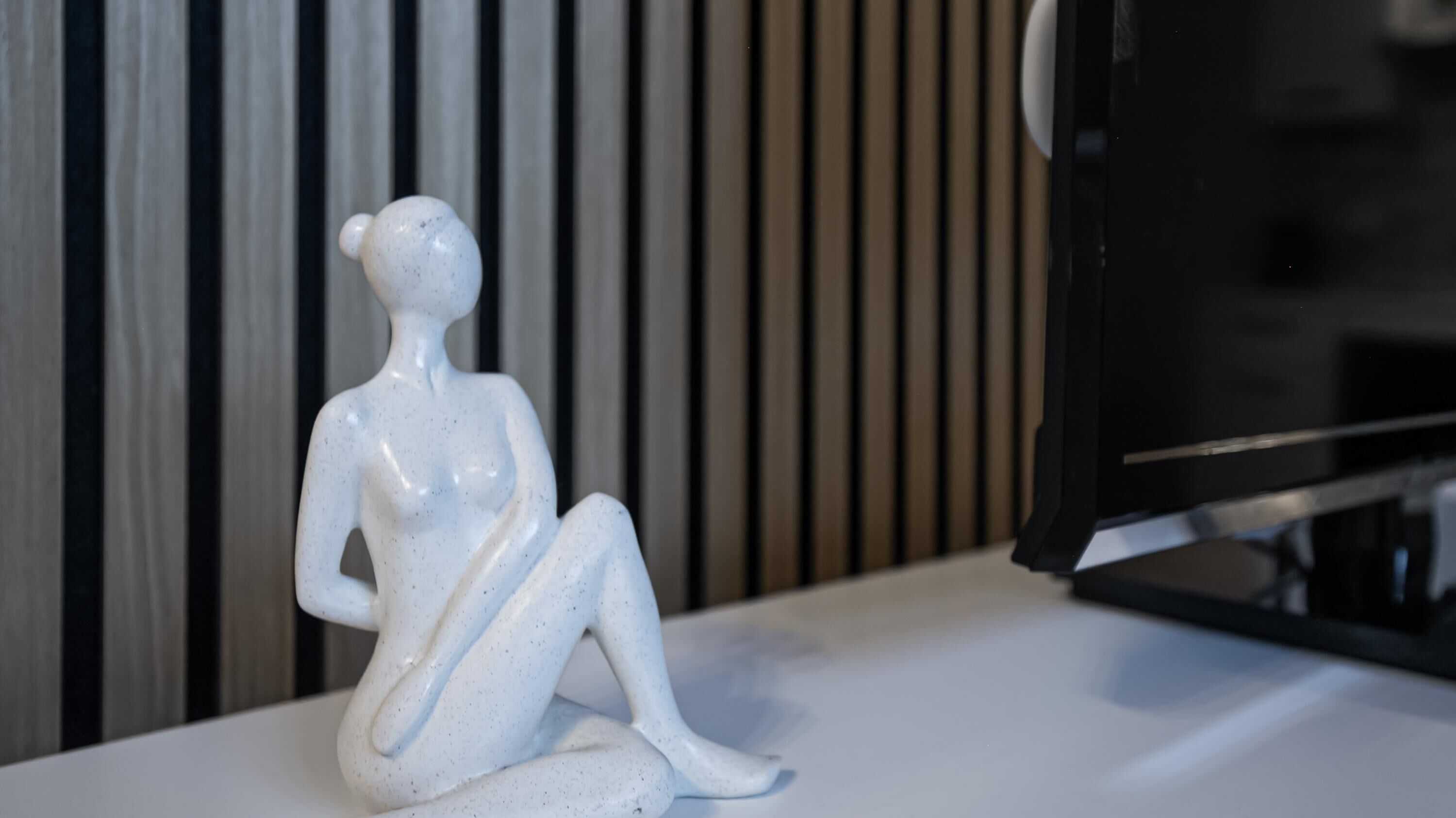 Een witte keramieken sculptuur van een zittend figuur op een wit oppervlak.