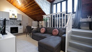 A modern kitchen with white cabinets, a dining area with a gray sofa and pink cushions, and a staircase with white railings. - Rovani 14 in Monza With 1 Bedrooms and 1 Bathrooms (Monza)