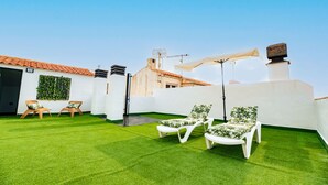 Une terrasse sur le toit avec un revêtement de gazon synthétique, des fauteuils blancs et un mur blanc agrémenté d’un mur végétal.